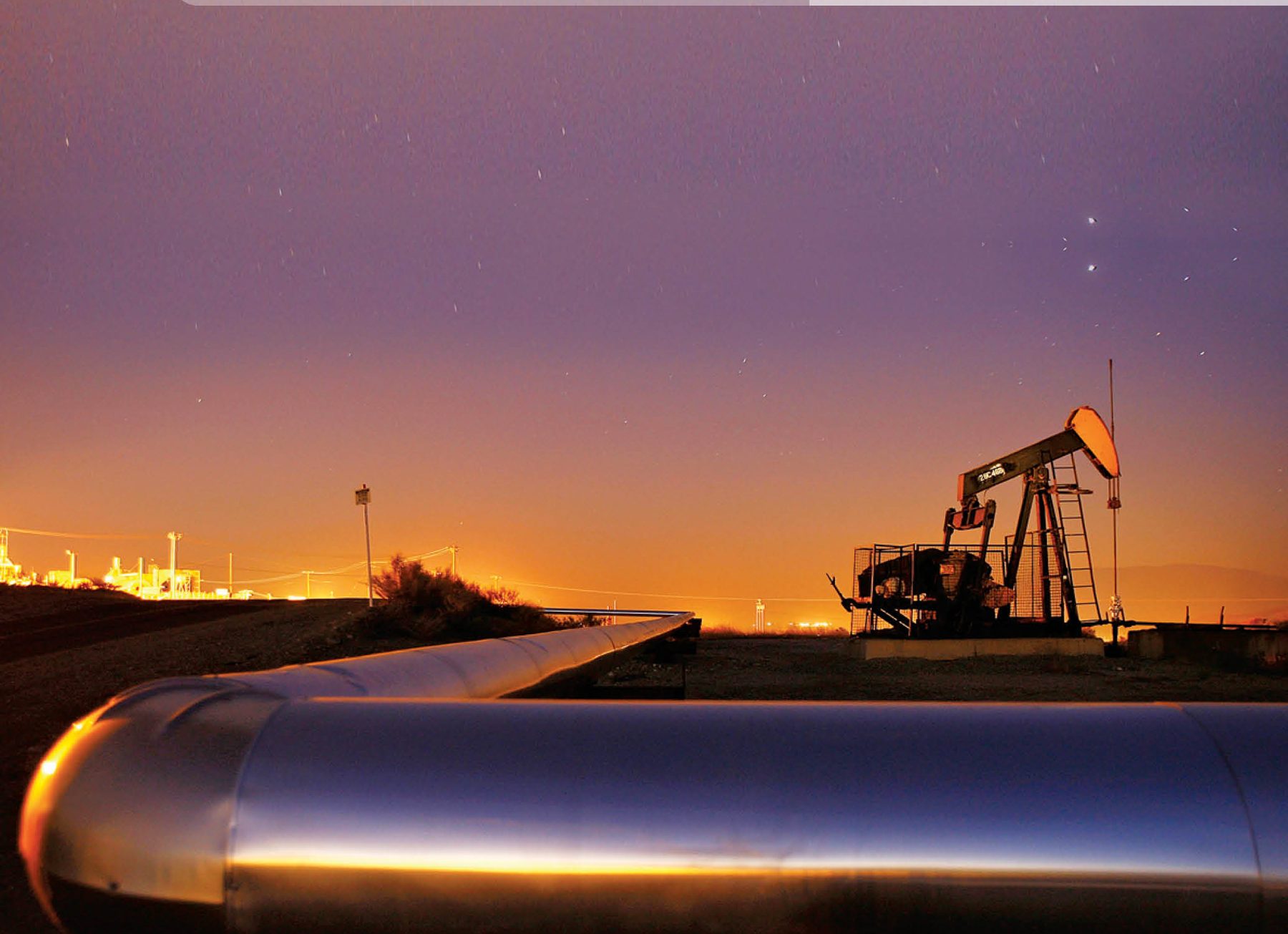 Oil pipeline and pump jack at sunset